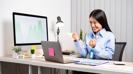 Asian woman working on a laptop with a cheerful and happy smile while working at the office