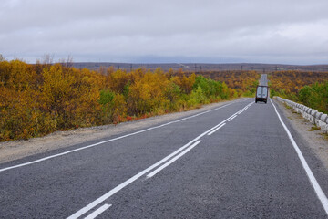Daytime traffic, autumn landscape. A road with a concrete safety barrier and a dividing strip.