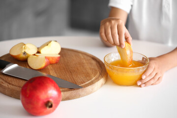 Little boy eating apple and honey at home. Rosh Hashanah (Jewish New Year) celebration