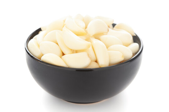 Close-Up of organic fresh peeled garlic (Allium sativum) in black ceramic bowl over white background