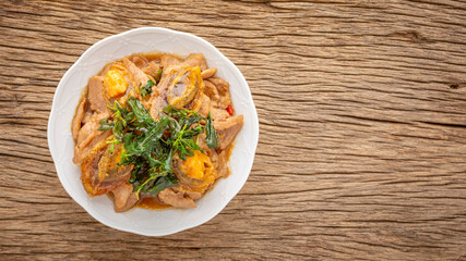Pad Ka Prao Kai Yeow Ma, Thai food, basil stir fried century egg and sliced pork with crispy basil leaves on top in ceramic plate on rustic natural wood texture background with copy space, top view
