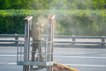 A worker removes old paint from road barriers using an air compressor. Roadside infrastructure...
