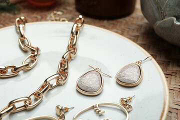 Stylish golden bijouterie on plate, closeup. Elegant jewelry