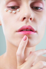 Close-up of beautiful young woman with pink makeup and pearls under eye keeping index finger near lips