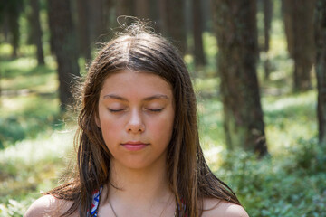 Portrait of a pretty teenage girl meditating and relaxing in nature against the background of a forest, prayer