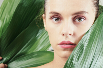 Naklejka premium Portrait of serious young Caucasian woman with natural makeup posing among tropical leaves