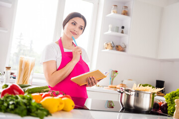 Photo of pretty thoughtful young lady wear pink apron cooking dinner thinking new recipe smiling indoors room home house