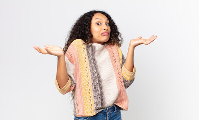 pretty hispanic woman shrugging with a dumb, crazy, confused, puzzled expression, feeling annoyed...