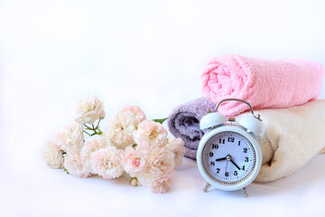 The concept of a good morning and a wonderful mood. Alarm clock, bath towels, pastel delicate roses on a light background, side view, space for text