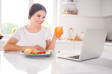 Photo of positive happy mature woman smile watch video laptop drink juice eat meal indoors inside kitchen