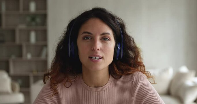 Happy confident young hispanic businesswoman in wireless headphones looking at camera, holding distant web call negotiations meeting. Beautiful millennial latin teacher recording educational video.