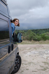 Portrait of a young woman leaning out of the window of a van. Vertical photo.