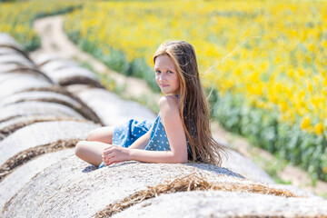 9 years old girl with long hair on top of the round hay bale looking to the camera. Happy summer time. Generation Z.