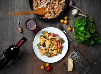 Colorful pasta with white meat and red wine on a dark grey table.