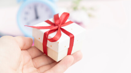 A girl in a white sweater holds a gift wrapped in craft paper with a red bow on a white background. Close-up, space for text.