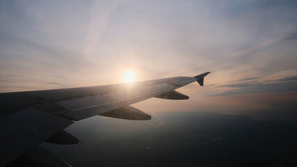 Fototapeta premium View from the porthole to the wing of the aircraft in flight. Sun and clouds over the wing of the aircraft at altitude
