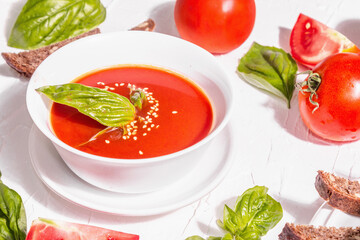 Bowls with homemade tomato soup. Ripe vegetables, fresh basil leaves, breadsticks, aromatic spices