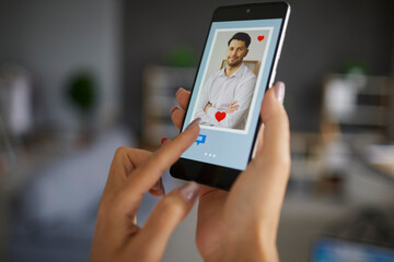 Female finger pushing chat button on smartphone using dating app to find love and online connection. Focus on handsome man profile photo on screen. Modern lifestyle relationship, remote relation