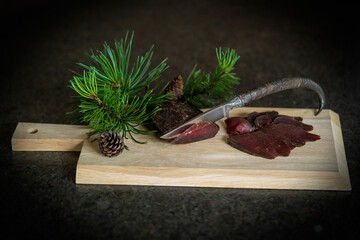 delicious ham of a chamois buck on the wood board with a hunting knife and a twig from the mountain pine