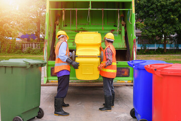 Two dustmen standing by a dustbin lorry emptying wheelie bins, Thailand