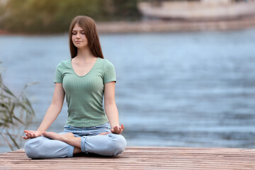 Fototapeta na wymiar Teenage girl meditating near river. Space for text