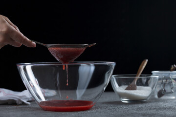 Woman straining strawberry jam through a sieve, home cooking and cooking concept