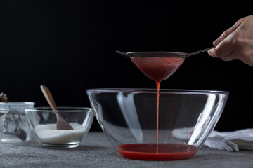 Woman straining strawberry jam through a sieve, home cooking and cooking concept