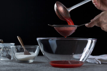 Woman straining strawberry jam through a sieve, home cooking and cooking concept