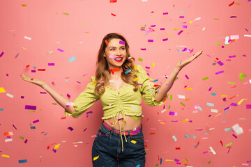 happy woman with outstretched hands near confetti on pink