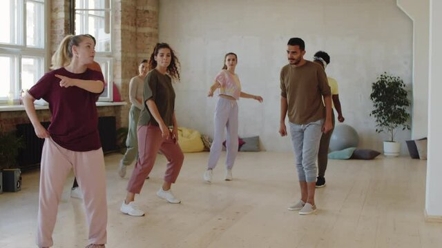 Group of young multiethnic men and women repeating dance moves with female trainer during class in studio