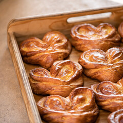 Baked sweet dough or pastry. Heart-shaped buns on wooden tray. Crispy snack or breakfast.