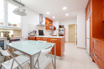 Large kitchen with cherry wood furniture with glass and metal office table with central island with white marble top in rental apartment
