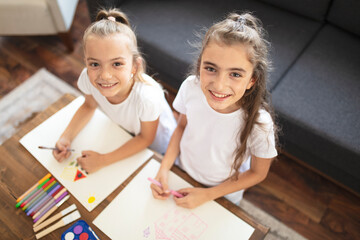 Happy little two sisters drawing at home.
