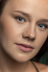Fototapeta premium Close-up young beautiful adorable girl's face isolated over dark green studio background. Natural beauty, wellness, well-kept skin, herbal cosmetics concept