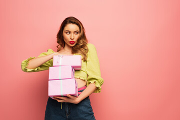 woman with duck face holding wrapped gift boxes isolated on pink