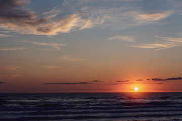Fototapeta premium Amanecer en la playa con vistas al Mar Mediterráneo con cielo anaranjado y nublado.