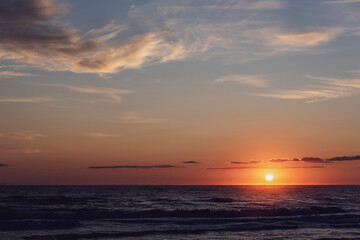 Amanecer en la playa con vistas al Mar Mediterráneo con cielo anaranjado y nublado.