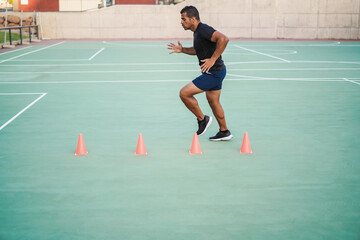 Hispanic man doing speed and agility cone drills workout session outdoors - Focus on man face