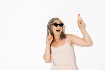 Senior woman wearing sunglasses laughing while pointing fingers upward