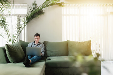 Young guy sitting at green sofa with gray laptop and black phone