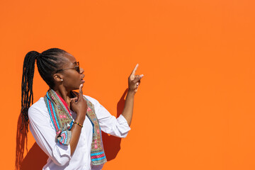 Empresaria africana con expresión de sorpresa señalando espacio para texto en fondo naranja.