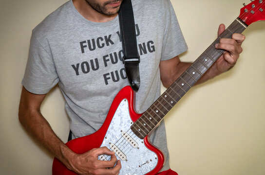 Young man with offensive t-shirt playing a red electric guitar.