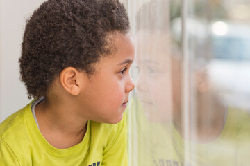 adorable sweet kid boy looking out the window, surprised and intrigued expression, waiting parents to come home or watching kids playing outside - 448977341