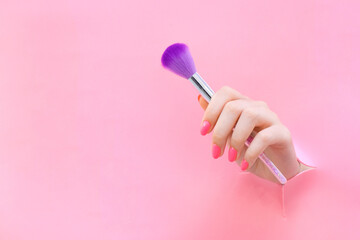 applying makeup, brush for manicure in the hand of a young woman on a pink background from a hole