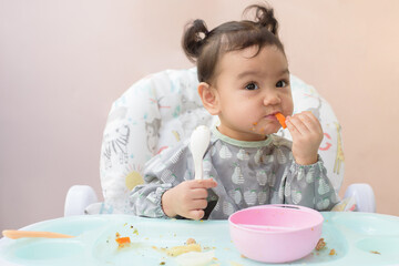 A cute Asian baby girl sitting on dining table practice eat carrot by her self, Baby-Led Weaning...