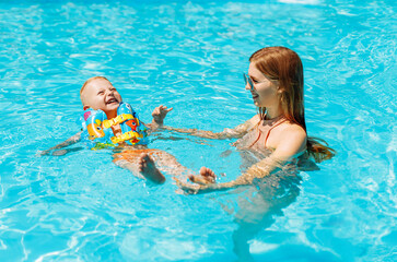 Happy family, mom and baby in inflatable vest swim and enjoy in the pool, have fun in the water on family vacation, Summer vacation