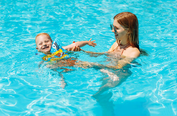 Fototapeta na wymiar Happy family, mom and baby in inflatable vest swim and enjoy in the pool, have fun in the water on family vacation, Summer vacation