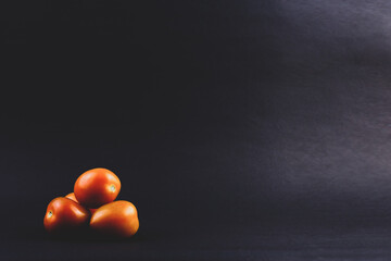 A few tomatoes are isolated on a dark and simple background. 