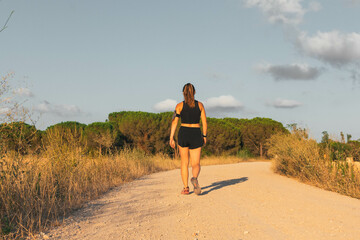 Rear view of a caucasian young woman walking in a mountain path during the golden hour.