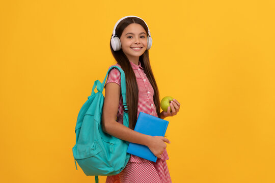 happy school kid in headphones carry backpack and workbook with apple for lunch, healthy lifestyle